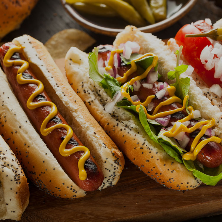 Hotdogs in poppy seed buns with mustard, onions and tomatoes