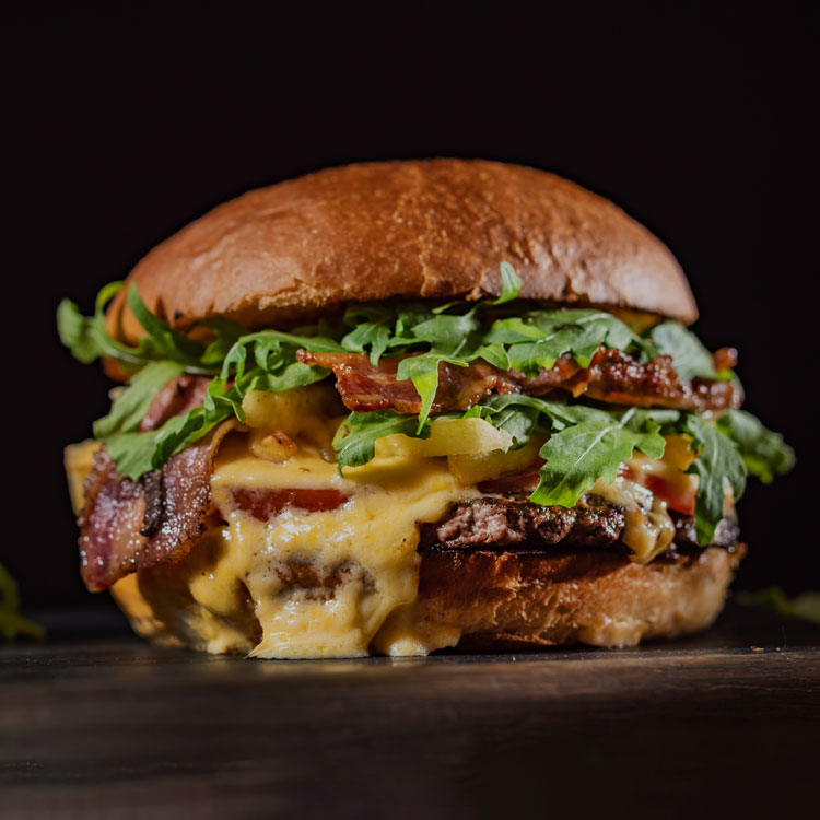 A beefburger with melted cheese, bacon and salad